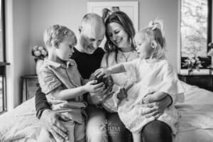 A family sit on the edge of a bed and hold their baby girl