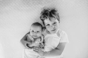 Newborn Photography: a little boy lays on a blanket cuddling his baby sister