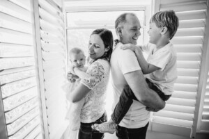 Newborn Photography: parents stand in front of a bright window cuddling their children
