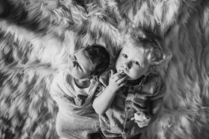 Newborn Photography: a little boy lays next to his baby brother on a fur blanket