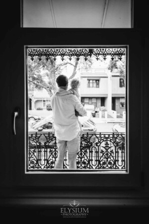 Newborn Photography: a father holds his little boy standing outside a window