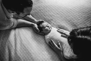 Newborn Photography: parents place their hands on their baby boy laying on a white blanket
