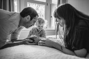 Newborn Photography: parents hold their baby laying on a white blanket