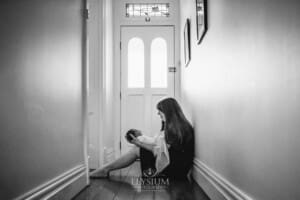 Newborn Photography: a mother sits in a hallway with her baby in her lap