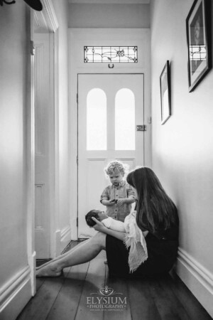 Newborn Photography: a mother sits in a hallway with her baby in her lap
