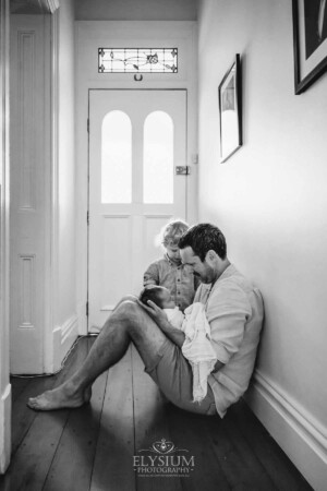 Newborn Photography: a father sits with his baby boys in a long hallway
