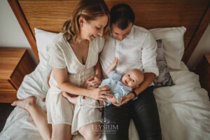 Newborn Photographer: parents sitting on a bed with their baby boy