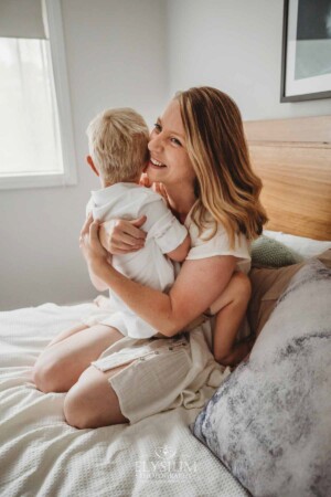 Newborn Photographer: a mother sits on a bed cuddling her little boy