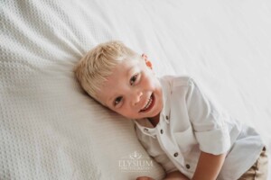 Newborn Photographer: a little boy lays on a white bedspread smiling