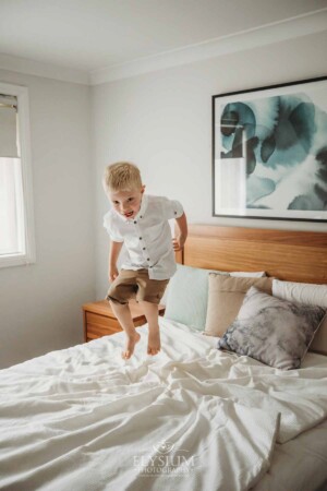 Newborn Photographer: a little boy jumps high on a white bedspread