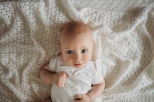 Newborn Photographer: a baby boy with blue eyes lays on a white blanket