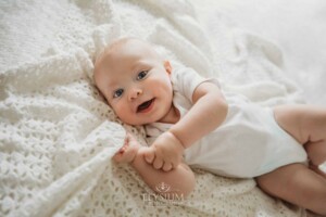 Newborn Photographer: a baby boy with blue eyes lays on a white blanket
