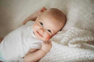 Newborn Photographer: a baby boy with blue eyes lays on a white blanket