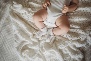 Newborn Photographer: baby boy with white booties lays on a white blanket
