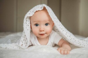 Newborn Photographer: a baby boy with blue eyes smiles under a white blanket