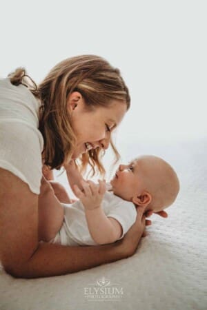 A mother smiles as she hugs her newborn baby boy laying on a white bed