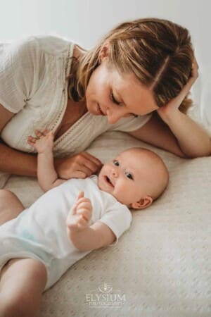 Newborn Photographer: a mother hugs her baby boy laying on a white bed