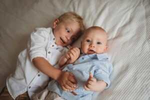 Newborn Photographer: a little boy lays on a bed cuddling his baby brother