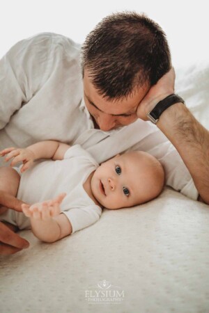 Newborn Photographer: a father hugs his baby boy laying on a bed