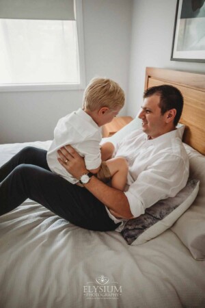 Newborn Photographer: a dad sits on a bed and bounces his son on his knee