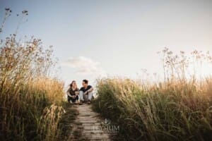 Engagement Photographer: a couple sit on a dirt path surrounded by long grass