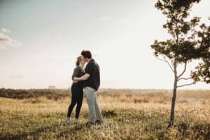 Engagement Photographer: a couple kiss on top of a hill at sunset