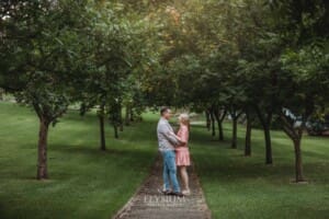 Engagement Photography: a couple stand hugging on a path through leafy green trees