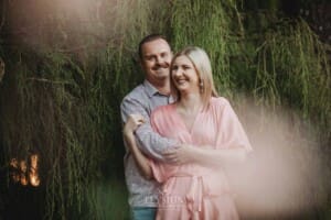 Engagement Photography: a couple stand cuddling against a green hedge
