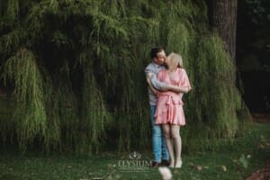 Engagement Photography: a couple kiss standing against a green hedge
