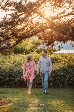 Engagement Photography: a couple walk hand in hand through gardens at sunset