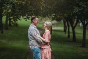 Engagement Photography: a couple stand hugging on a path through leafy green trees