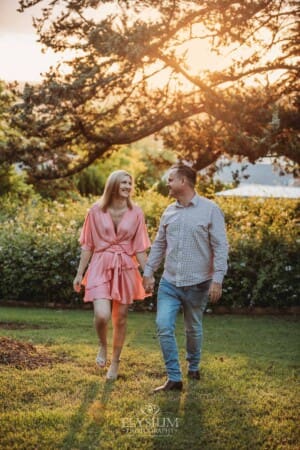 Engagement Photography: a couple walk hand in hand through a garden at sunset