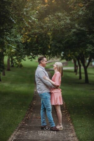Engagement Photography: a couple stand hugging on a path through leafy green trees