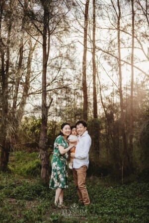 A family cuddle their baby boy between then in a forest