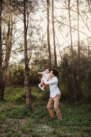 A dad spins his baby boy around in a forest at sunset