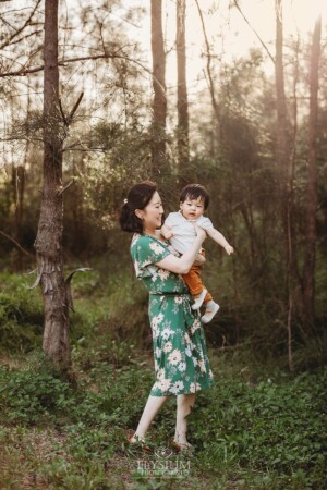 A mum spins her baby around in a forest at sunset