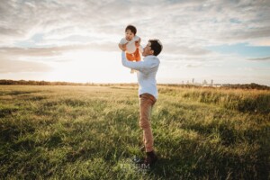 A father spins his baby around on a grassy hill