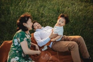 A baby sits on his dad's lap in long grass