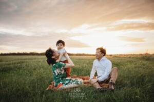 A family sit on a grassy hilltop with their baby at sunset
