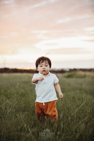 A baby boy walks through long grass at sunset