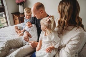 A family sits on a bed holding their newborn baby