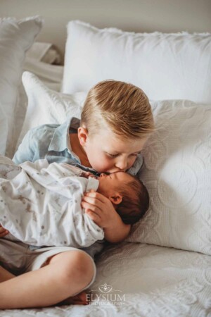 A little boy kisses his baby sisters head