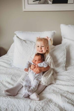 A little girl holds her baby sister in her lap