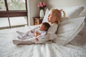 A little girl holds her baby sister in her lap