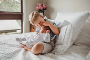 A boy kisses his newborn sister on the head