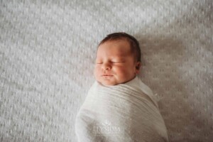 A newborn baby girl lays sleeping in a white wrap on a bed