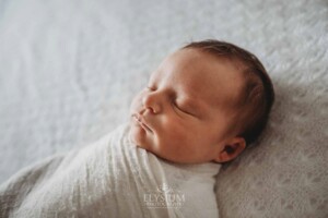 A newborn baby girl lays sleeping in a white wrap on a bed