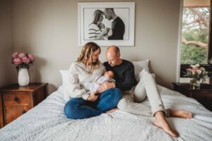 Parents sit on a bed and hold their baby girl between them