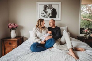 Parents sit on a bed and hold their baby girl between them