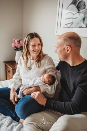 Parents sit on a bed and hold their baby girl between them